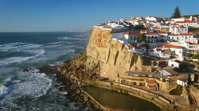 Azenhas do Mar is a fishing village located on a cliff by the Atlantic Ocean in Portugal. The coastal landscape shows the village along the rugged coastline and ocean waves