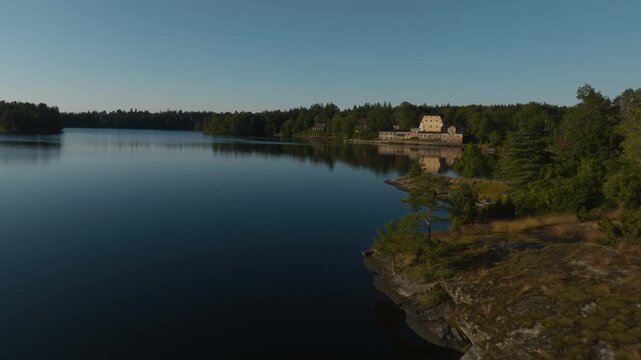 Drone shot passing a rocky shoreline revealing a classic Swedish-style estate and old church