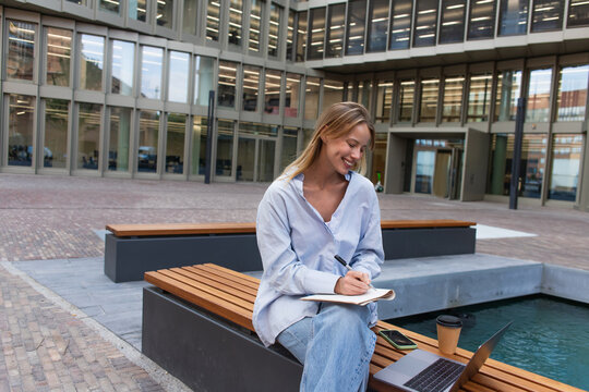 A beautiful young woman sits outdoors, jotting down notes while enjoying the city