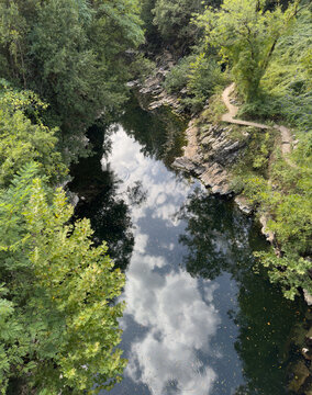 Small mountain river with reflections of the sky in calm water, surrounded by a lush green summer forest.