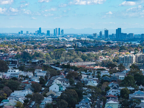 Aerial view of suburban housing and lush greenery with a distant metropolitan skyline under a clear blue sky in Parramatta, New South Wales, Australia.