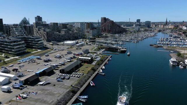 Marina and harbor channel lined by boats and modern buildings in Aarhus docklands up and coming bustling region, Denmark, aerial establishing overview