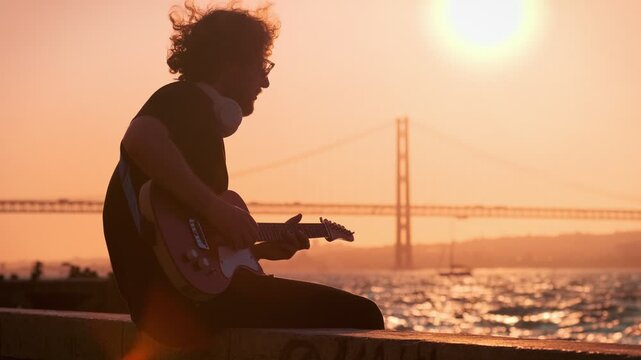 Street musician in black plays an electric guitar outdoors at sunset