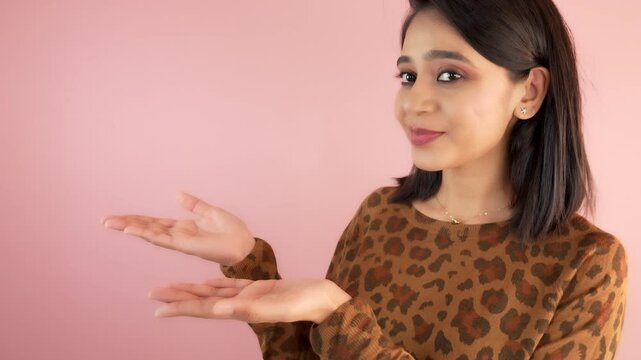 Portrait of a young woman pointing at something show empty space advertisement look at camera, isolated against pink colour studio background.
