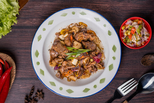 A serving of *ati ampela gongso* (stir-fried chicken liver and gizzard) on a plate, accompanied by *sambal dabu*, photographed against a gray background.