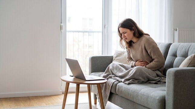 Young woman suffering from stomach pain while sitting on sofa