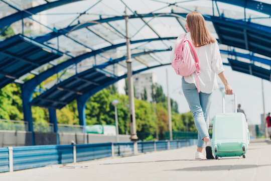 Young woman traveling with suitcase and backpack at urban railway station on a sunny day