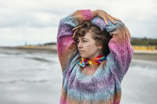 A confident girl stretches on the beach in a rainbow sweater