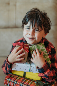 Boy holding a stack of Christmas gifts indoors