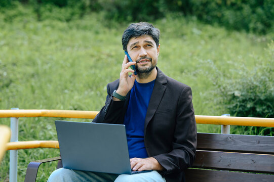 Businessman talks on phone while working on laptop in the park