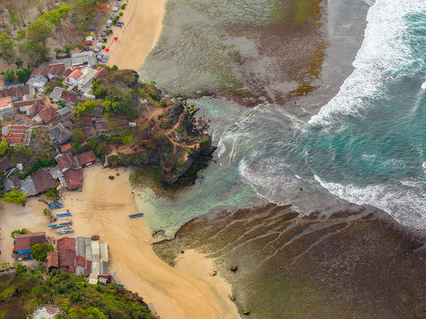 Aerial view of the coastal village in Gunungkidul Regency with traditional houses, sandy beach, rocky cliffs, and small fishing boats in Special Region of Yogyakarta, Indonesia.