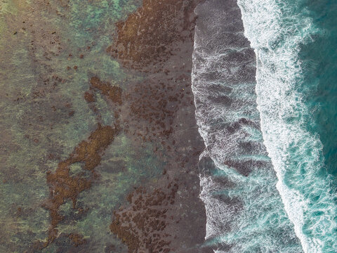 Aerial view of the rugged coastline of Gunungkidul Regency with turquoise ocean waves crashing against dark rocky reefs, Special Region of Yogyakarta, Indonesia.