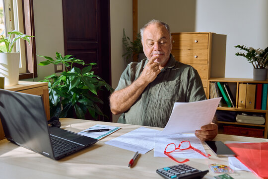 Senior man reads financial document at home office desk