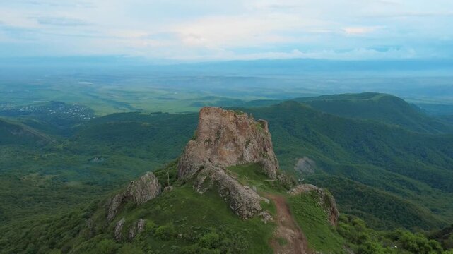 Aerial drone shot slowly flying away from the ancient kojori fortress ruins, also known as azeuli or korogli, perched on a dramatic mountain peak overlooking a vast, lush green valley in georgia