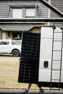 Worker carrying solar panel for PV system installation outdoors