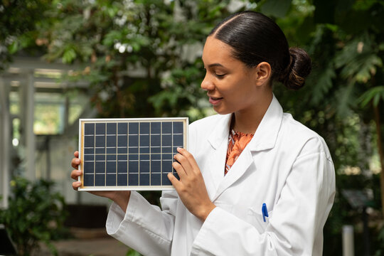 Female scientist holds a solar panel in a lush greenhouse