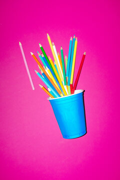 A blue cup holds colored pencils on a pink background