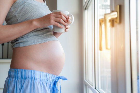 Close-up of pregnant woman holding cup at the window