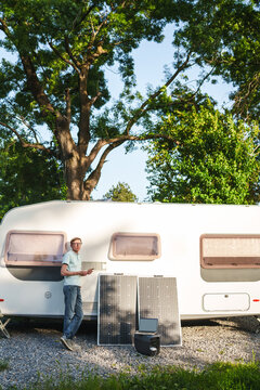 Man at campsite uses solar panel to charge battery and work online