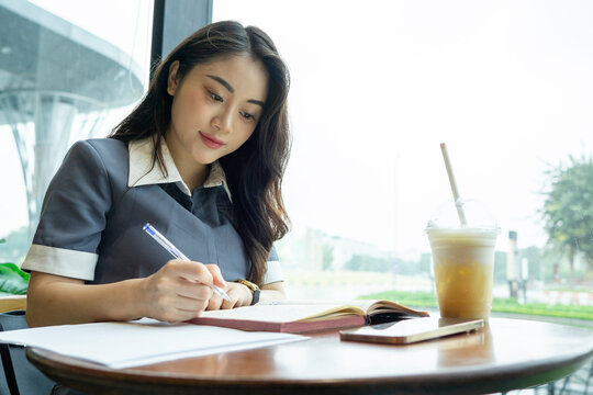 A focused woman is writing in a notebook at an outdoor cafe