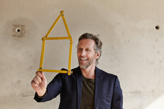 Smiling man holding pocket rule in shape of a house