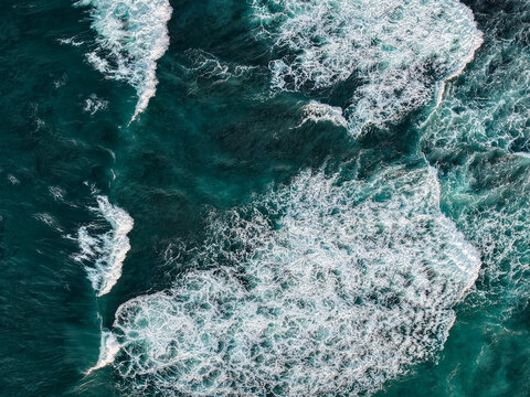 Aerial view of ocean waves crashing against the coast with white sea foam and deep blue water in Gunungkidul Regency, Special Region of Yogyakarta, Indonesia.
