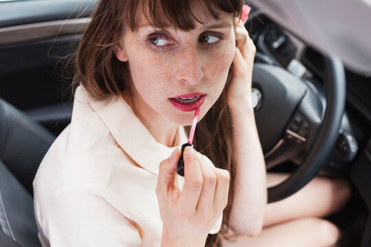 Portrait of businesswoman sitting in her car applying lipstick