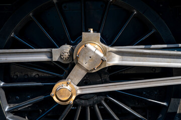 Detailed close-up of a large black driving wheel, polished connecting rods and motion mechanism of a steam locomotive at Grosmont, North Yorkshire, England. © ON-Photography