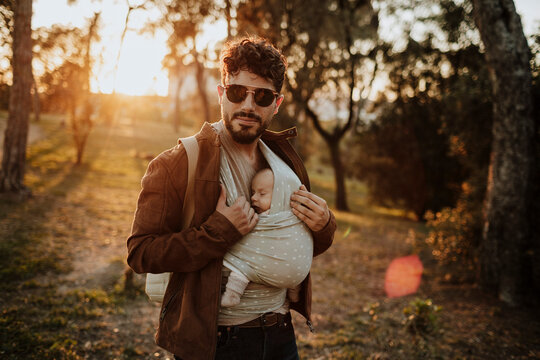 Confident father carries his sleeping baby boy outdoors at sunset