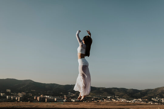A female dancer performs a graceful jump above the Barcelona skyline