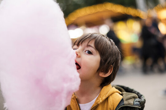 A young boy eats pink cotton candy outdoors at a fair