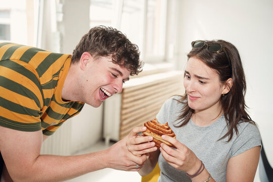 Young man playfully steals a sweet pastry from his female friend
