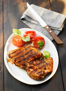 A grilled steak with tomato sits on a plate outdoors
