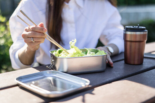 Businesswoman eats a healthy salad from a reusable lunchbox outdoors