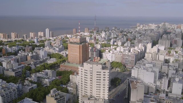 Aerial view of the Intendencia de Montevideo building surrounded by urban streets, lush trees, and the Rio de la Plata in the background in Montevideo, Montevideo, Uruguay.