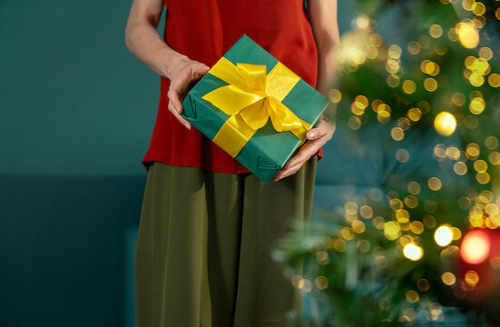 Woman holds a wrapped Christmas gift at home near a festive tree