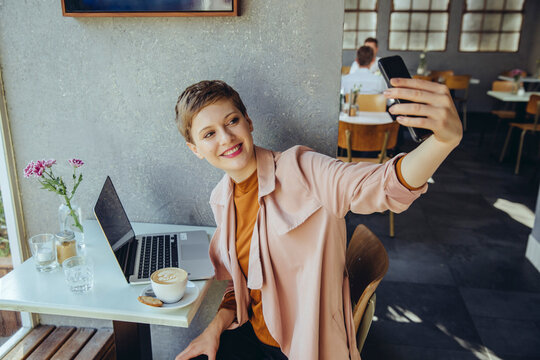 Woman taking a selfie with coffee and laptop in cafe