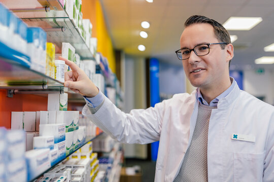 Portrait of smiling pharmacist with medicine at shelf in pharmacy