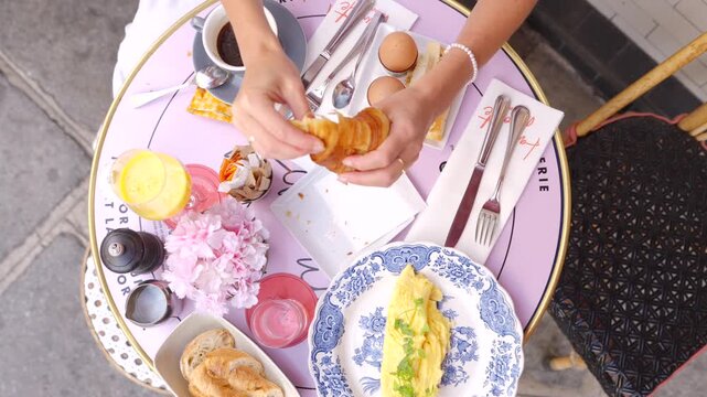 Overhead view of woman breaking croissant at Paris cafe breakfast