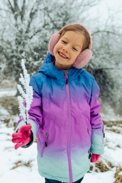 A smiling girl in a winter jacket holds a snowy branch outdoors