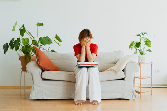 Stressed woman covers her face while sitting on a sofa indoors