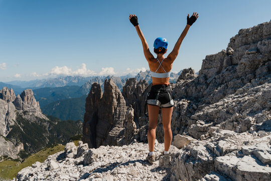 A joyful woman raises her arms on a mountain peak in the Dolomites