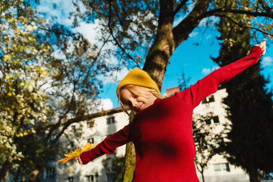 Carefree girl stretches arms holding autumn leaf outdoors