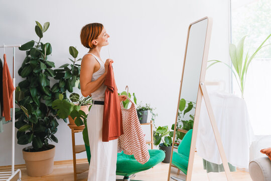 A smiling woman chooses a shirt in front of a mirror at home