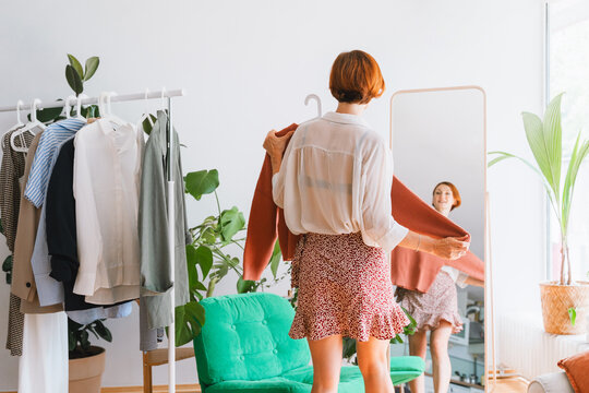 Happy woman trying on a terracotta sweater in front of a mirror