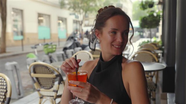 Smiling woman stirring orange cocktail on Paris cafe terrace