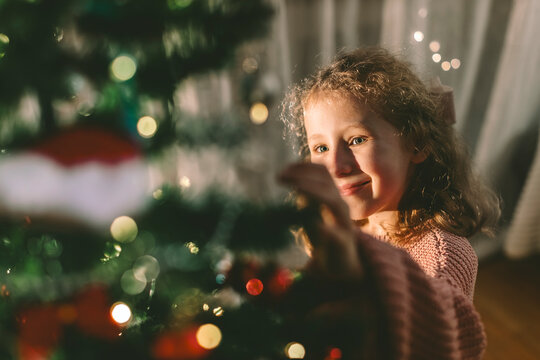 A smiling girl decorates a Christmas tree at home in the evening