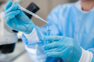 Close-up of scientist hands in blue gloves using a pipette to drop liquid into a test tube in...