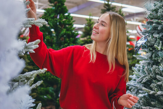 A woman in a red sweater chooses a Christmas tree in a store