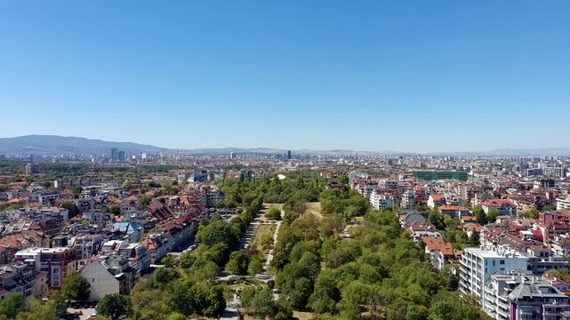 Aerial view of Geo Milev Park surrounded by urban residential buildings and lush green trees under a clear blue sky in Sofia, Sofia City Province, Bulgaria.